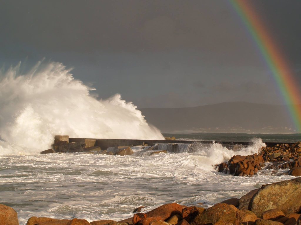 Ola rompiendo fuerte contra protección del puerto mientras forma un arcoiris, caSAnosa